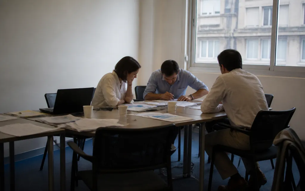 Trois adultes en stage intensif d’anglais autour de documents étalés sur la table