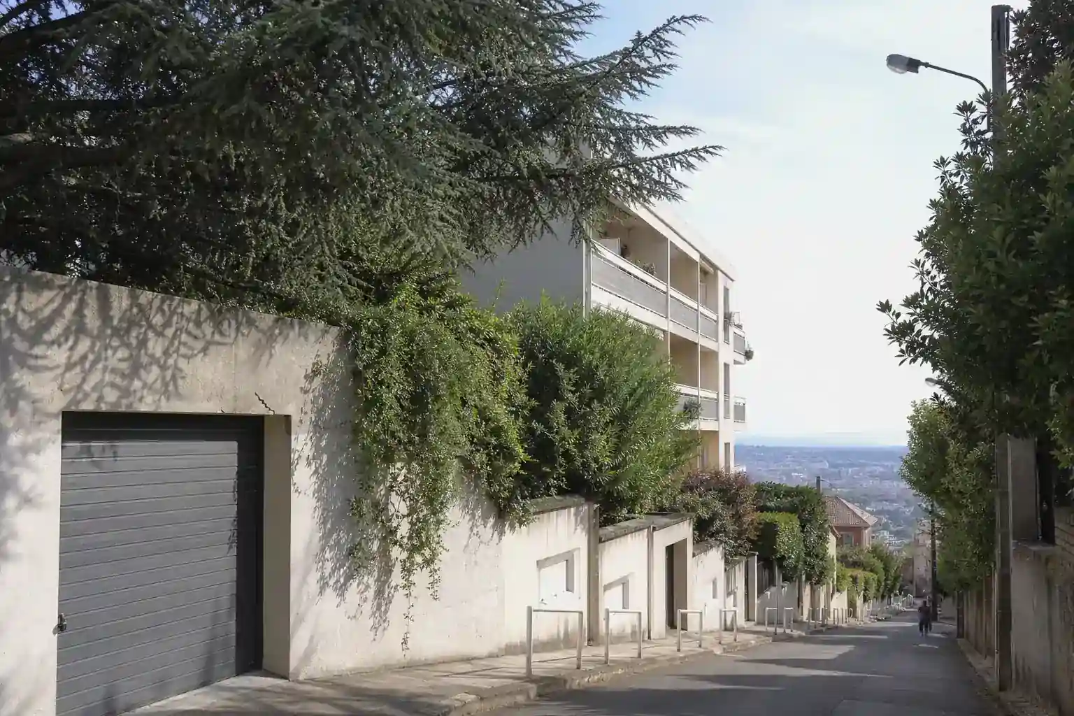 Rue résidentielle en pente à Caluire-et-Cuire, murs de clôture et arbres