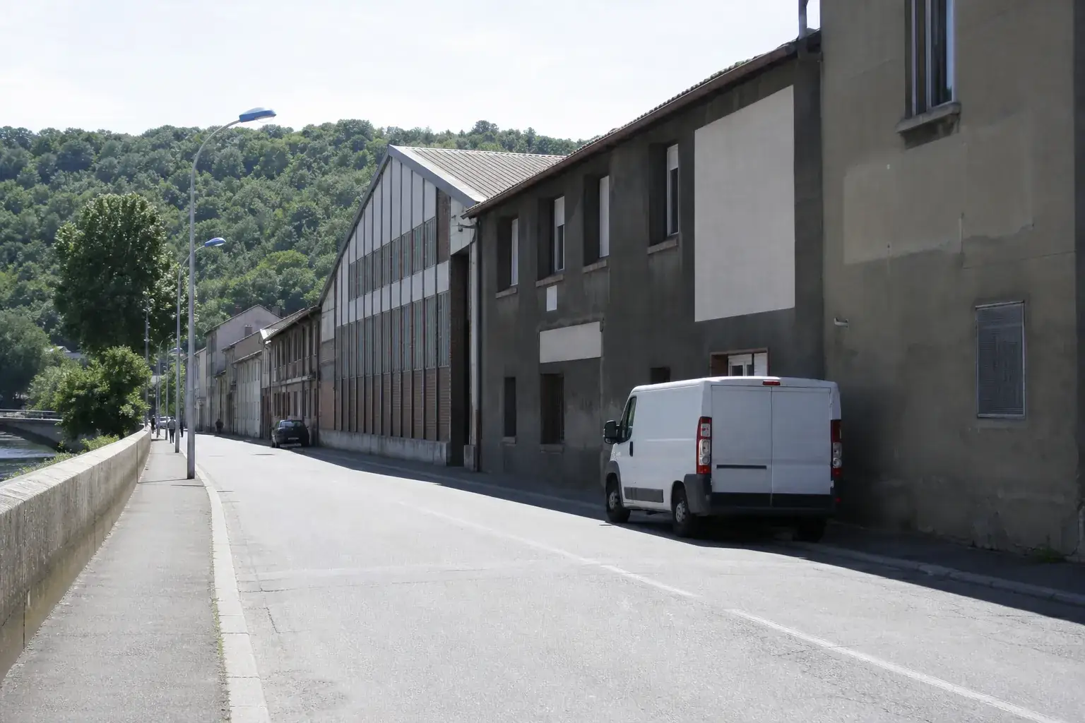 Rue de Givors à midi, bâti ouvrier ancien et coteau boisé en arrière-plan
